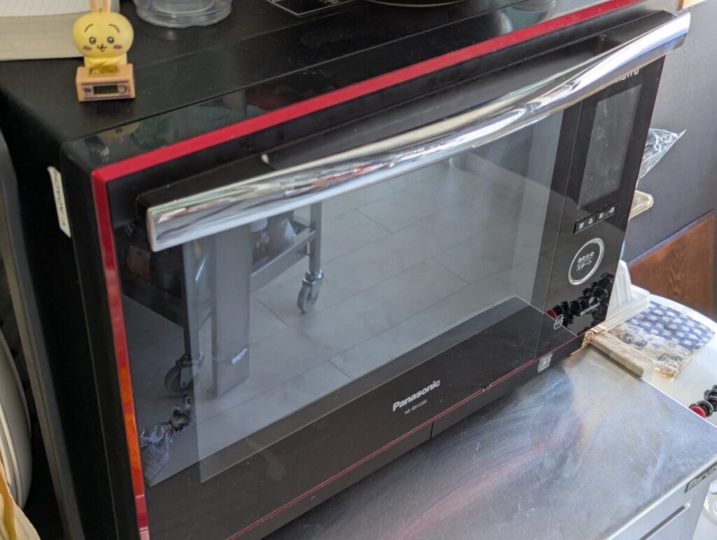 Panasonic製の黒と赤のオーブンレンジ。前面ガラス扉と大型ハンドルが特徴で、デリピックスのオープンサンドをグリルモードで調理する際に使用された。