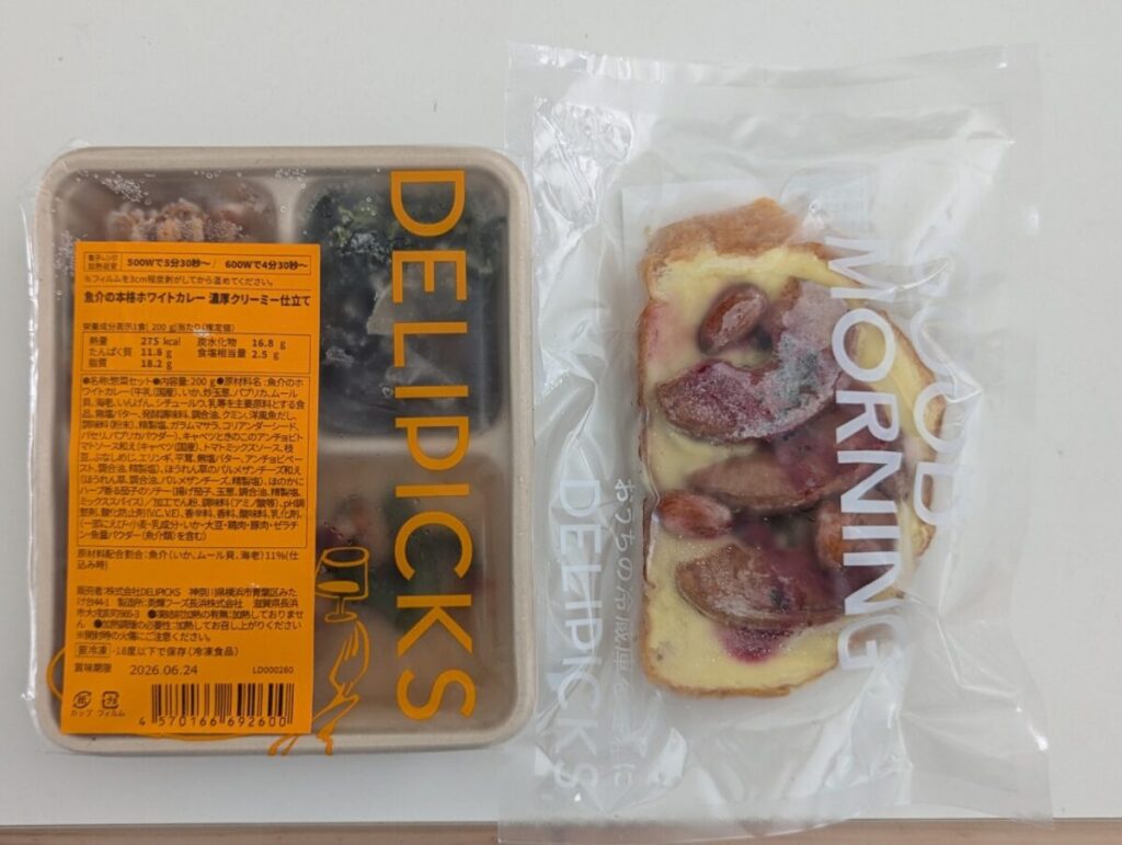 DELIPICKSの冷凍おかずセットと、フルーツ入りオープンサンドをテーブルに並べた写真。パッケージラベルが見えるように撮影されている。