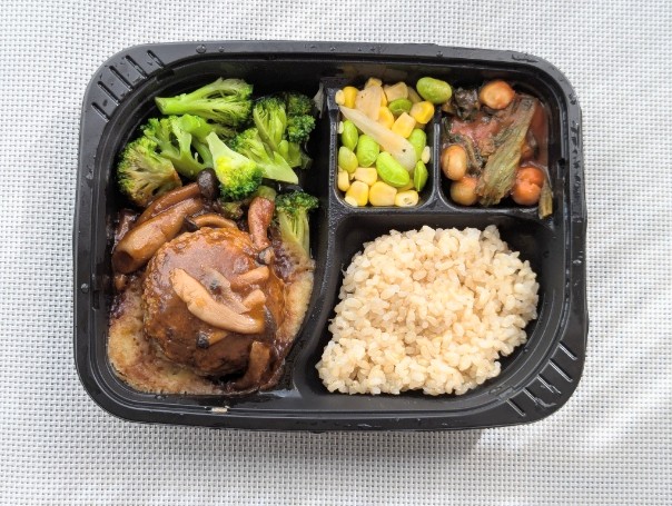 筋肉食堂DELIの冷凍弁当「赤ワイン香るきのこのデミグラスソースと肉厚ビーフハンバーグ」。ジューシーなハンバーグにきのこのデミグラスソースをかけ、付け合わせにブロッコリー、枝豆とコーン、豆のトマト煮、副菜と玄米ごはんが添えられている。