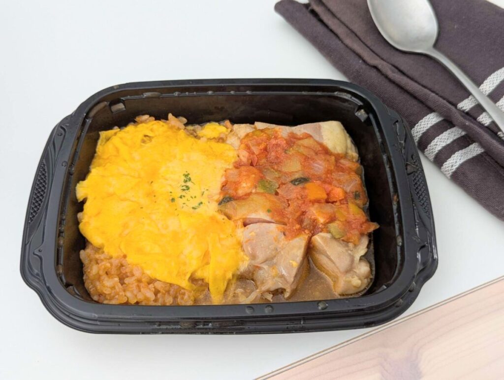 筋肉食堂DELIの冷凍弁当「完熟トマトのラタトゥイユとローストチキン＆とろふわミニオムライス」。ジューシーなローストチキンにトマトのラタトゥイユソースをかけ、とろふわ卵のオムライスを添えた一品。黒い容器に盛り付けられている。