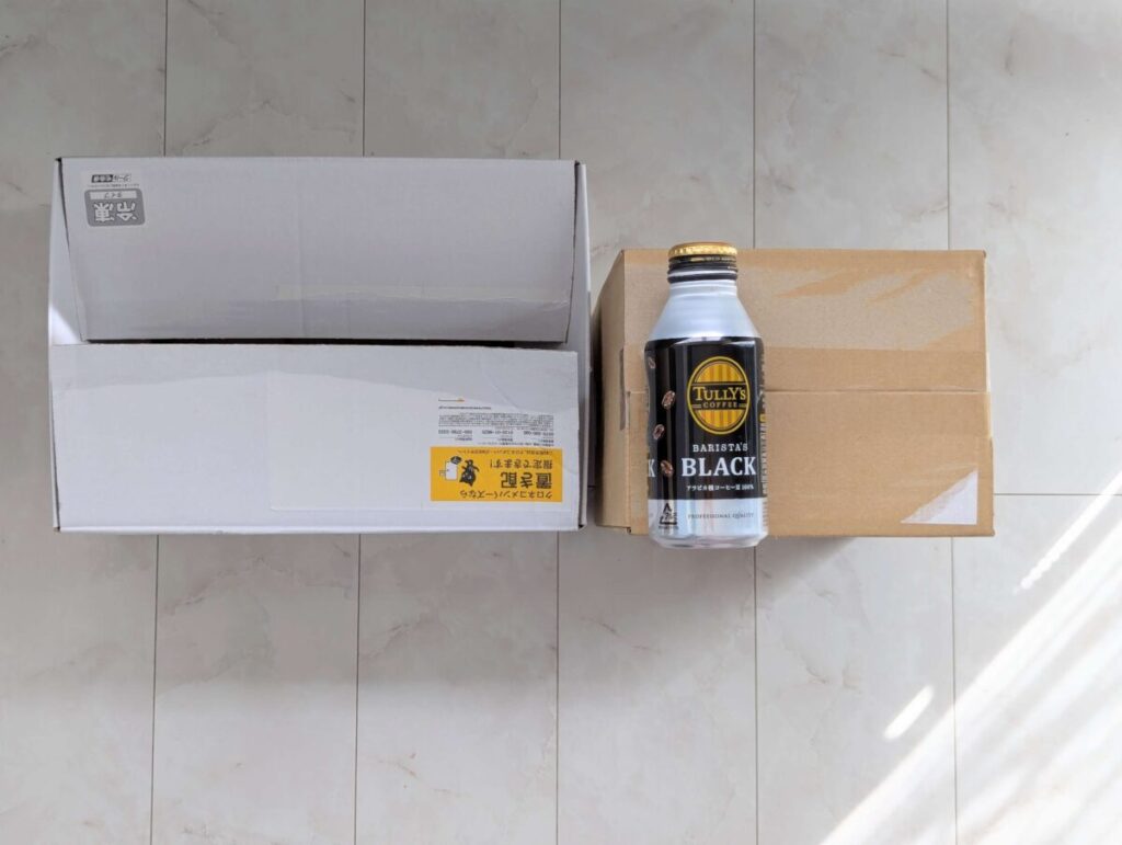 白い大きめのMuscle Deliの段ボール箱と、茶色の小さめの筋肉食堂DELIの段ボール箱を並べた写真。サイズ感の比較用にタリーズコーヒーの缶ボトルが右側に置かれている。