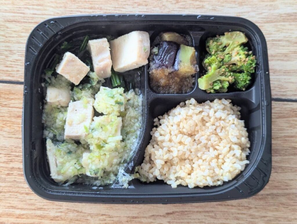 筋肉食堂DELIの冷凍弁当「しっとり蒸し鶏とネギたっぷりの特製塩ダレ」。角切り蒸し鶏に香味ネギ塩ダレをかけたメインに、揚げなすのおろし和え、ブロッコリーの胡麻和え、玄米ごはんがセットになっている。