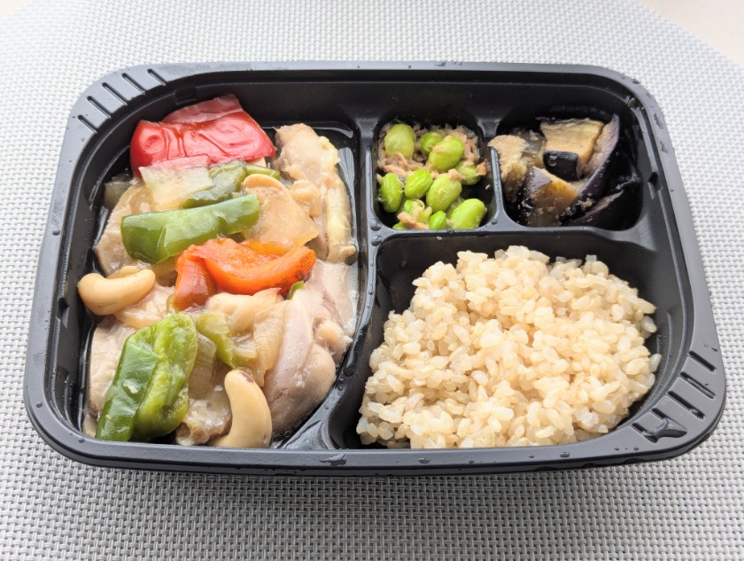 筋肉食堂DELIの冷凍弁当「鶏もも肉のカシューナッツ炒め」。大きめの鶏肉とパプリカ、ピーマン、カシューナッツを炒めたメインに、枝豆とツナの副菜、揚げなすの副菜、玄米ごはんがセットになっている。