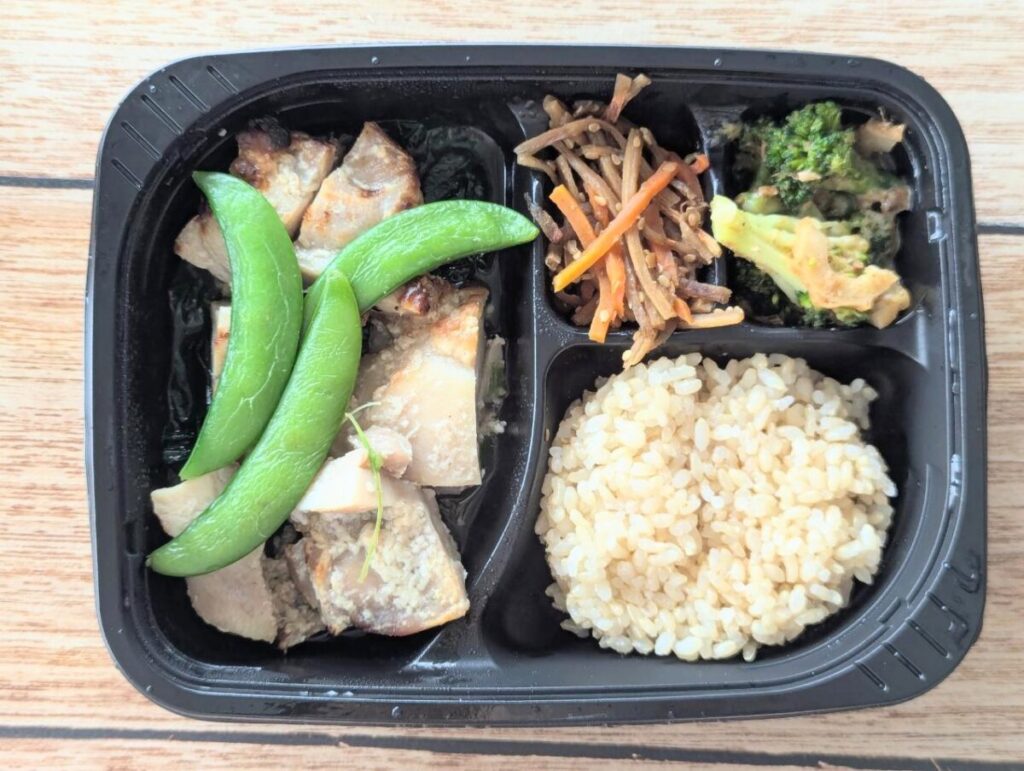 筋肉食堂DELIの冷凍弁当「じわっと旨味しみこむ鶏もも肉とスナップエンドウの塩こうじ焼き」。塩こうじでしっとり焼き上げた鶏もも肉にスナップエンドウを添え、副菜にはきんぴらごぼう、ブロッコリーのおかか和え、玄米ごはんが入っている。