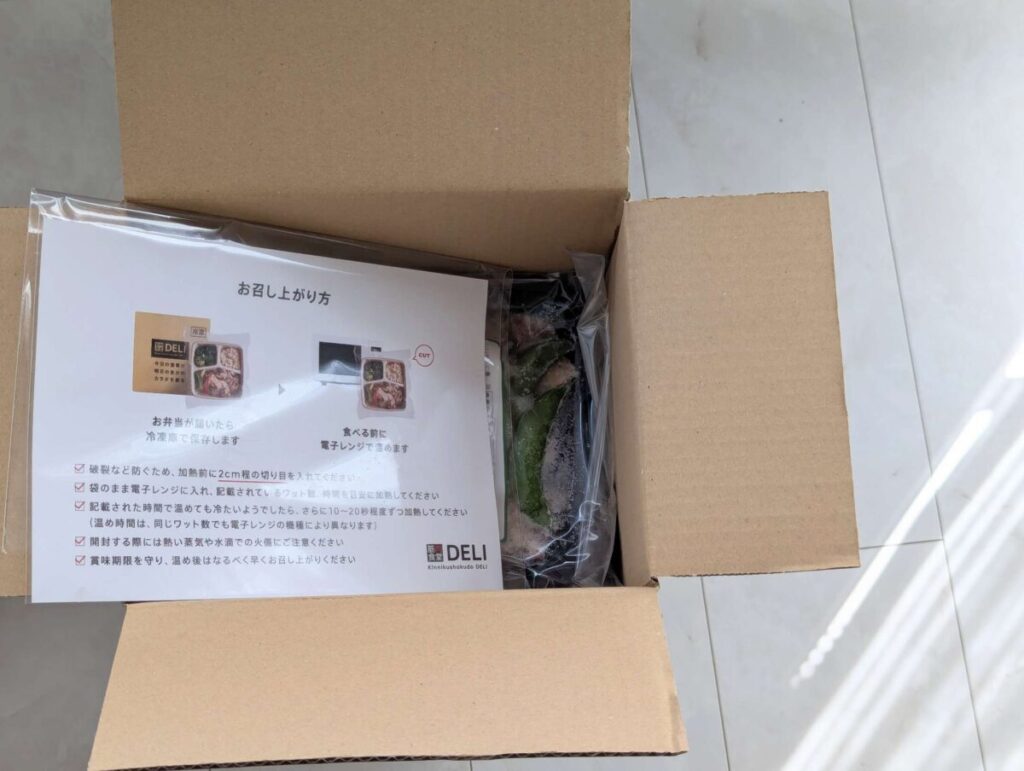 筋肉食堂DELIの段ボールを開けたところ。中には冷凍弁当と一緒に「お召し上がり方」が書かれたリーフレットが同梱されており、電子レンジでの温め方や保存方法が記載されている。