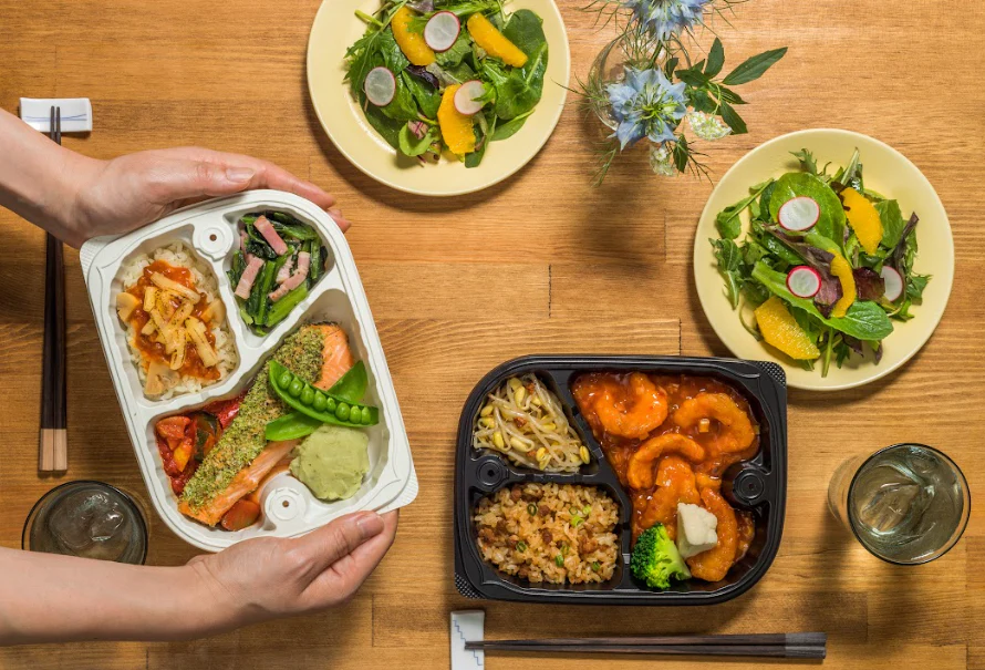 Oisie Dining（オイシエダイニング）の宅配食メニュー。サラダとセットになった彩り豊かな洋風と中華風のお弁当がテーブルに並んでいる。