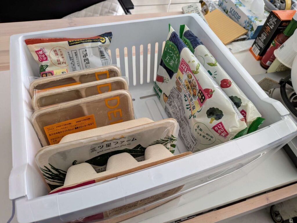 16.8Lの冷凍室に、ワタミの宅食ダイレクト「いつでも三菜・五菜」とデリピックス、三ツ星ファームのトレーを縦に並べて収納している様子。三菜は奥、五菜は右側に立てて入っており、冷凍庫の占有スペースがわかる。