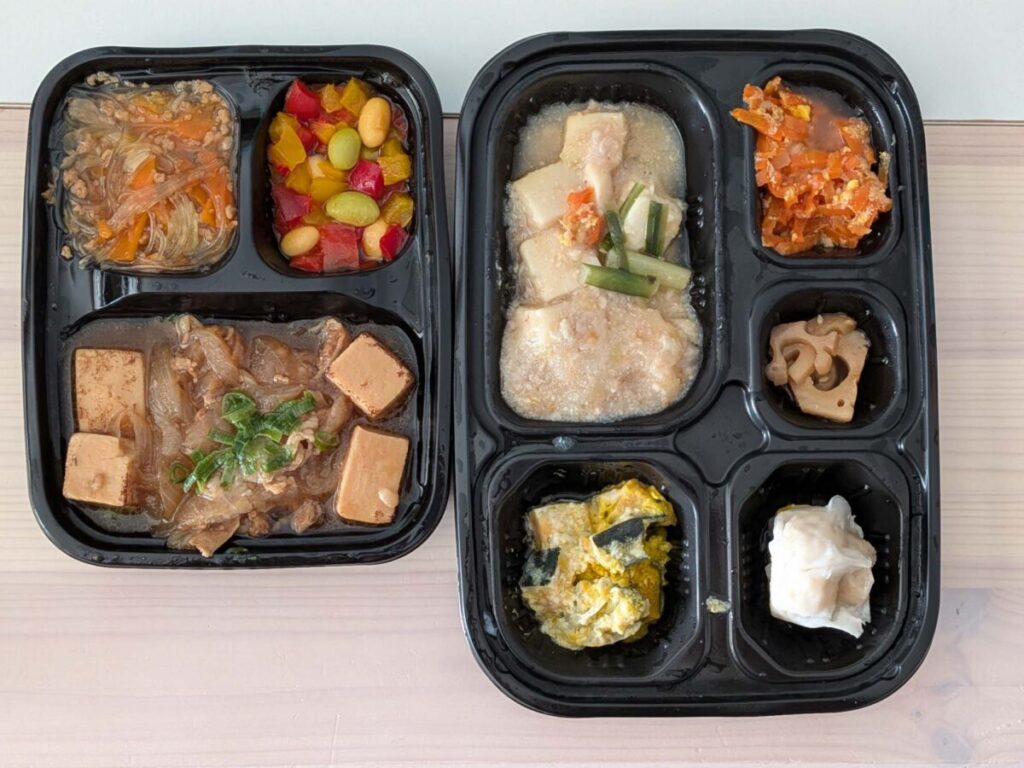 ワタミの宅食ダイレクトの三菜『牛肉と焼き豆腐の煮物』と、五菜『鍋仕込みの麻婆豆腐』を並べた写真。三菜は焼き豆腐と牛肉の煮物・春雨の副菜・パプリカ豆サラダの3品、五菜は麻婆豆腐・人参しりしり・れんこん煮・かぼちゃサラダ・焼売の5品が黒いトレーに入っている様子。