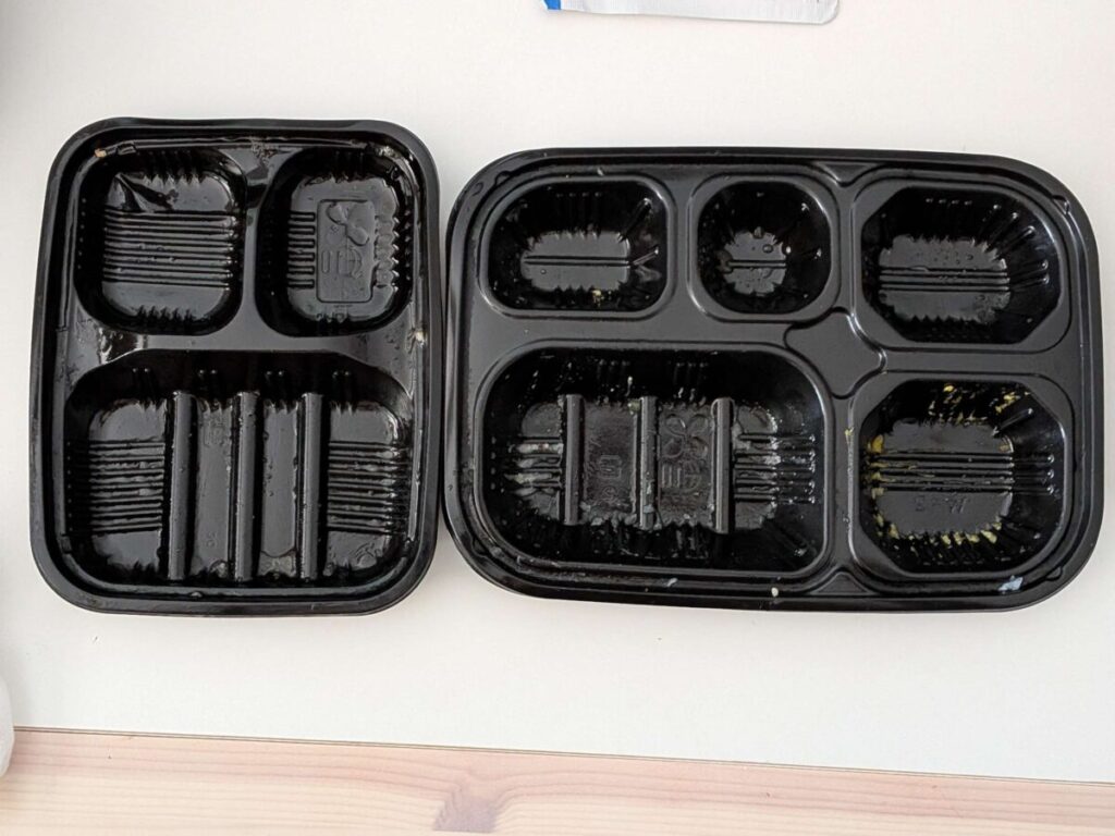テーブルの上に並べたワタミの宅食ダイレクトの空トレー。左が3マスの「いつでも三菜」、右が5マスの「いつでも五菜」で、仕切りの数やトレーの横幅の違いがわかる。