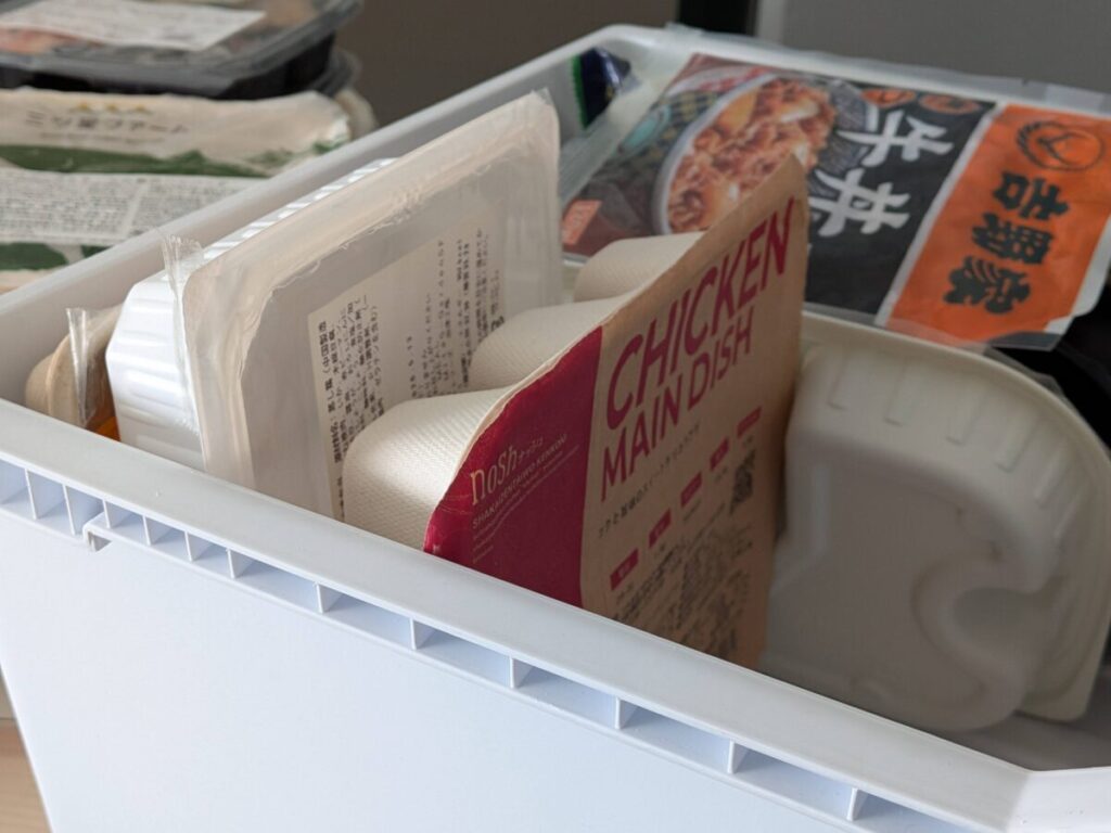 冷凍庫に収納されたナッシュとマッスルデリなど複数の冷凍弁当パック。立てて入れることでスペースを有効活用している様子。