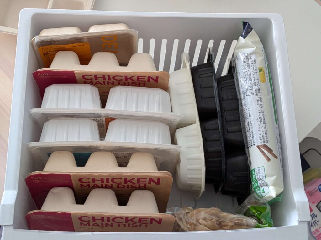 冷凍庫にナッシュやマッスルデリの冷凍弁当を立てて収納している様子。複数の容器が重ねずに整理されている。