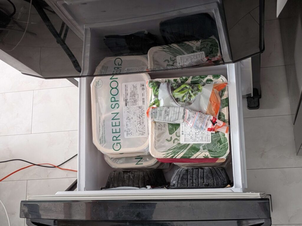容量20.5Lの冷凍庫に、GREEN SPOON（グリーンスプーン）のデリ弁当、他社の宅配食3食、さらに上に冷凍野菜の袋を重ねて収納している様子を上から撮影した写真