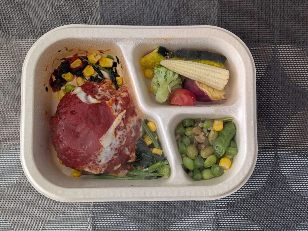 グリーンスプーンデリ弁当チーズとろける完熟トマトハンバーグ。サイドは枝豆ガーリックペッパー と温野菜サラダ