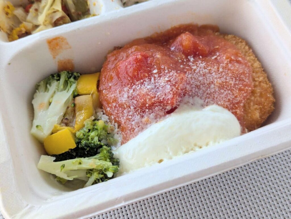 三ツ星ファームのカニクリームコロッケアップ写真。左に付け合わせのブロッコリーと黄ズッキーニ。カニクリームコロッケにはトマトソース、チーズソース、パン粉がかかっている。