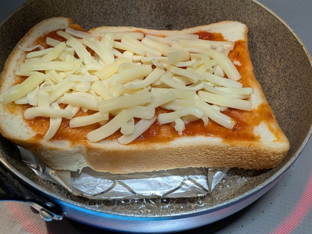 アルミホイルの土台に乗せた冷凍パンの脇に、小さじ1〜2の差し水をしている様子。ホイルシートの堤防があるため、パンが濡れる心配がありません。