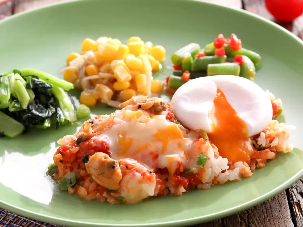 ナッシュのとろ～り半熟卵のトマトリゾットを緑色のお皿に盛り付けた様子。副菜は、小松菜ソテー、えのきコーンサラダ、インゲンの玉葱ドレッシング和え。